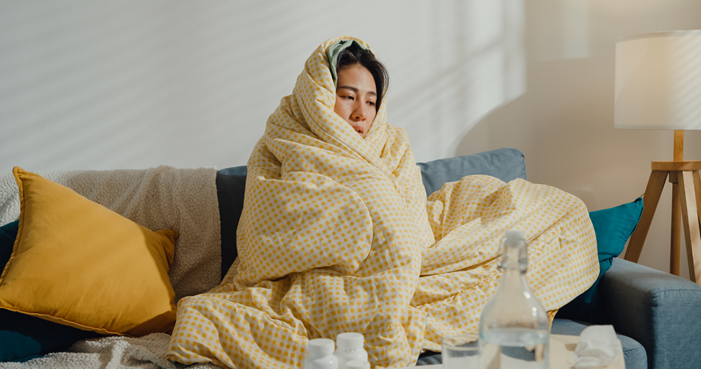 A woman with a stuffy nose wrapped in a duvet on her couch